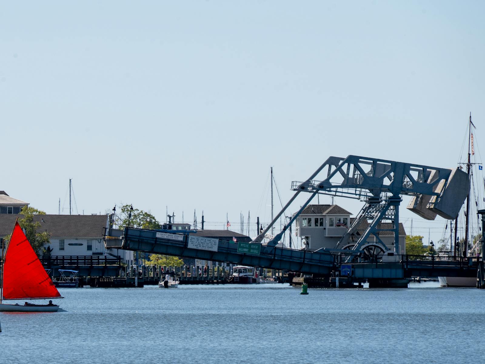 Mystic River drawbridge raised over the water with a red sailboat in Mystic, Connecticut